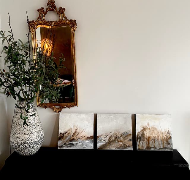 Drie kleine abstracte kunstwerken onder een sierlijke spiegel